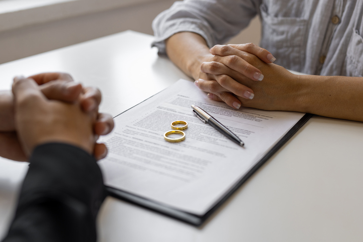 Two people sitting across from each other with wedding rings sitting on top of documents